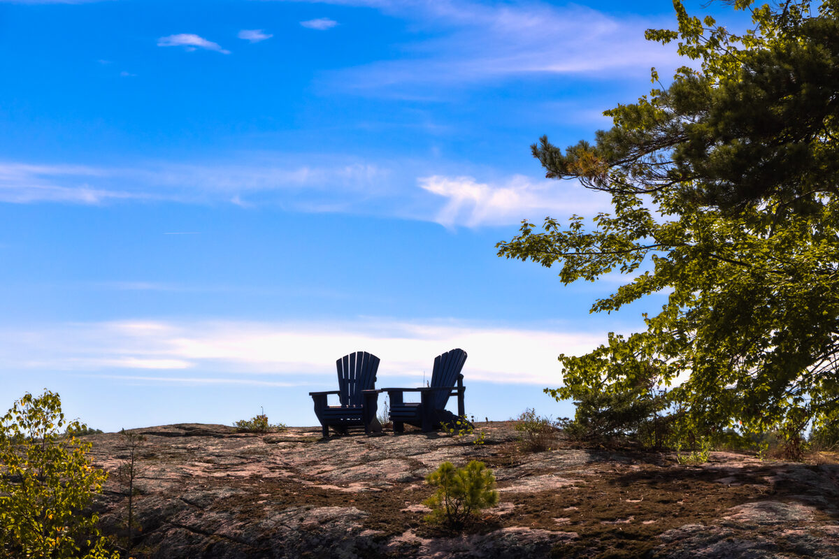 Two Adirondack chairs on a rocky point overlooking the calm Kawartha lakes at dusk