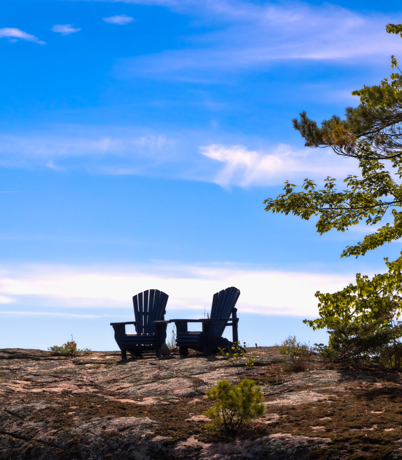 Two Adirondack chairs on a rocky point overlooking calm Kawartha water